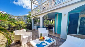A covered outdoor patio with white furniture and a dining table set for two, surrounded by tropical plants. - Princess Anaelle · Beachfront, Lage Pool, Privacy, Orient Bay, Deluxe 2 BDR (SAINT MARTIN)