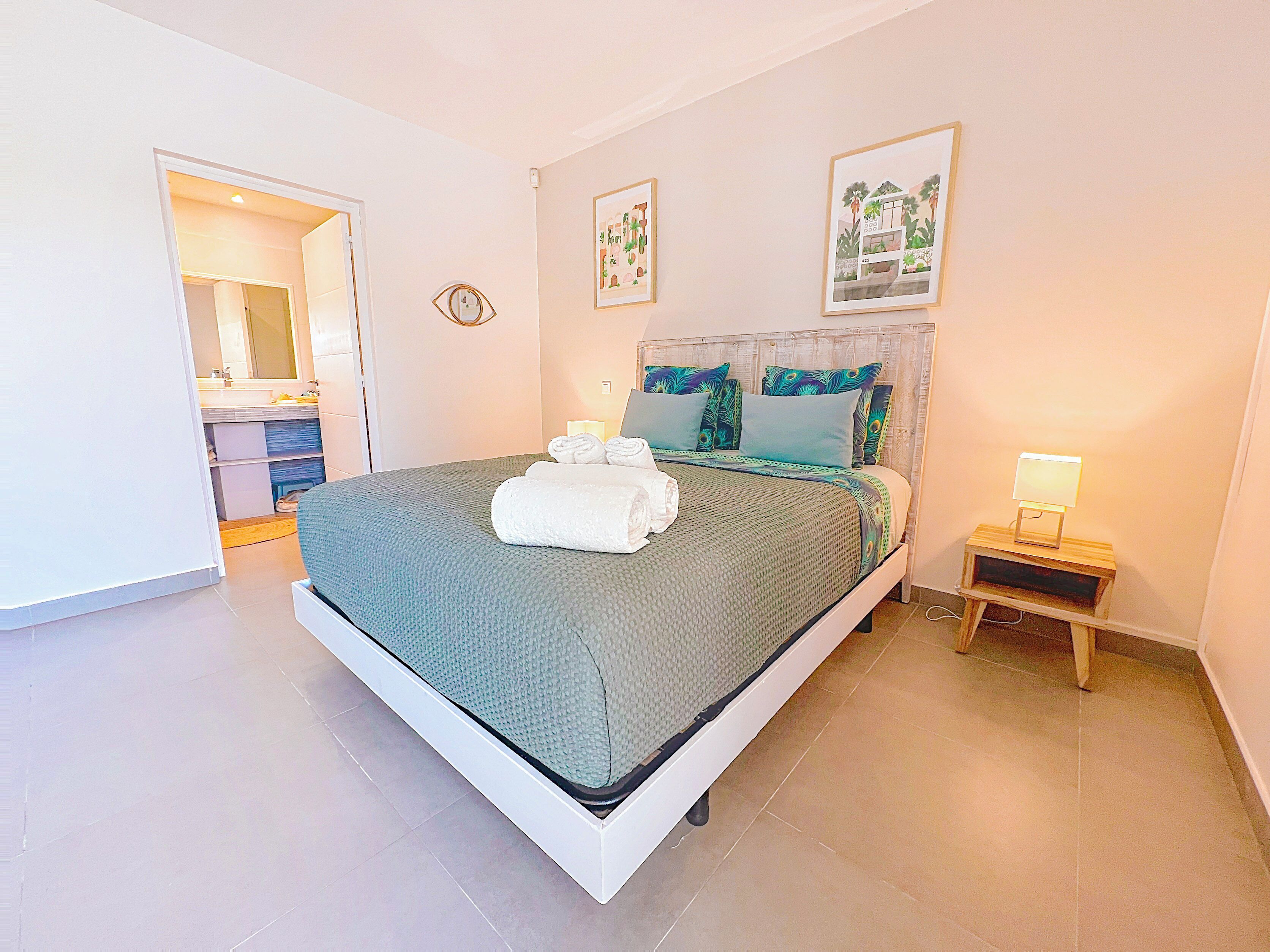 A neatly arranged bedroom with a bed, bedside table, and a small nightstand with a lamp.