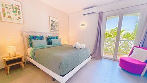 A bedroom with a bed, a nightstand, a chair, and a balcony with a view. - Princess Anaelle · Beachfront, Lage Pool, Privacy, Orient Bay, Deluxe 2 BDR (SAINT MARTIN)