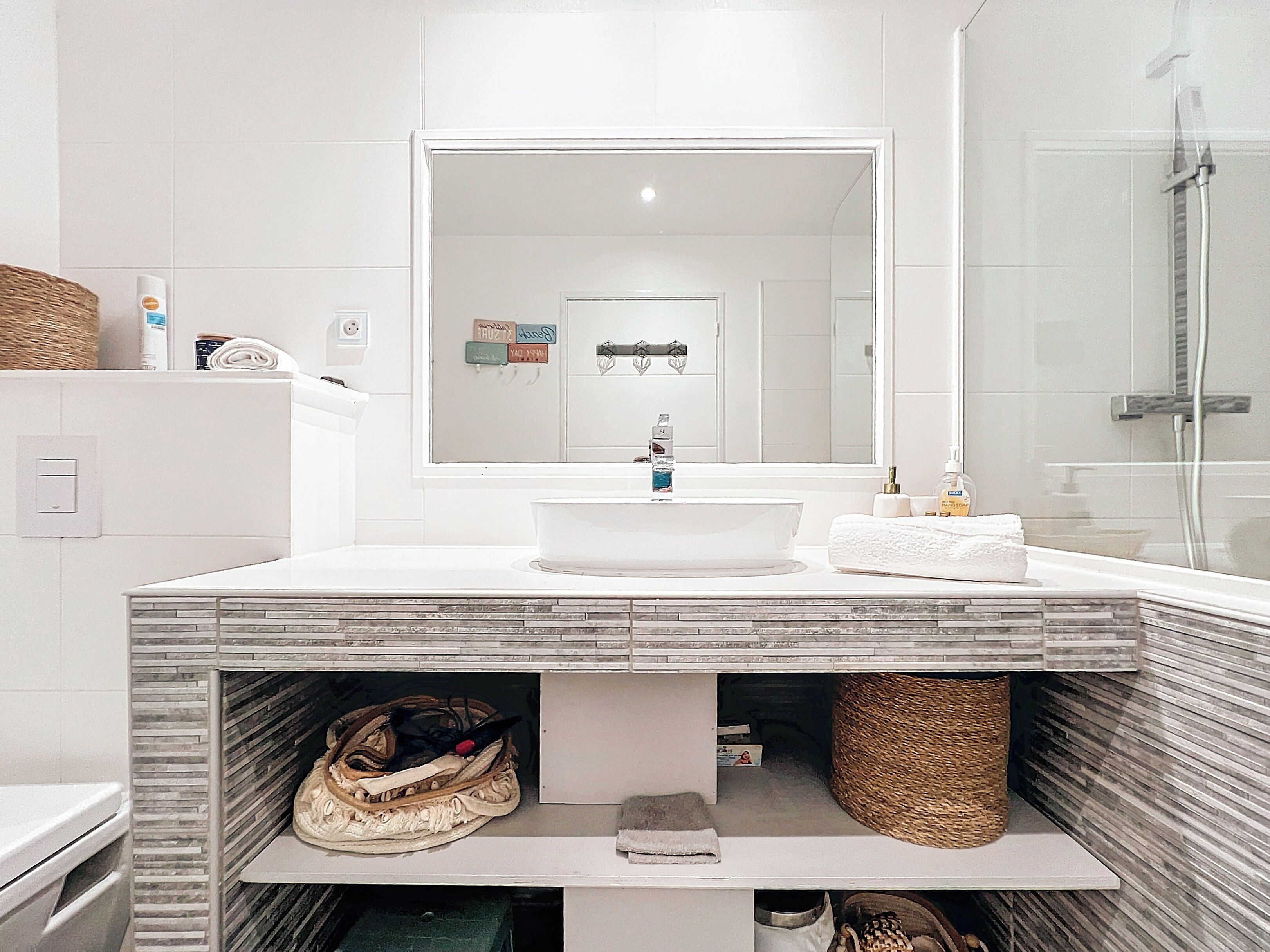 A modern bathroom with a large mirror, white sink, and a shower area.