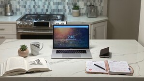 A kitchen with a laptop on a marble countertop, a book, a notebook, and a mug.