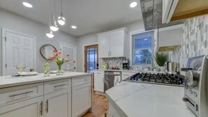 A modern kitchen with white cabinets, a central island, stainless steel appliances, and pendant lighting.
