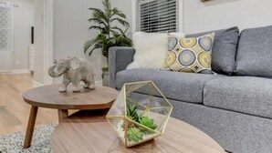 A modern living room with a grey sofa, patterned cushions, a wooden coffee table, a glass terrarium, and a decorative elephant figurine.