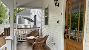 A porch with wicker furniture, a wooden door, and a covered area with a table and chairs.
