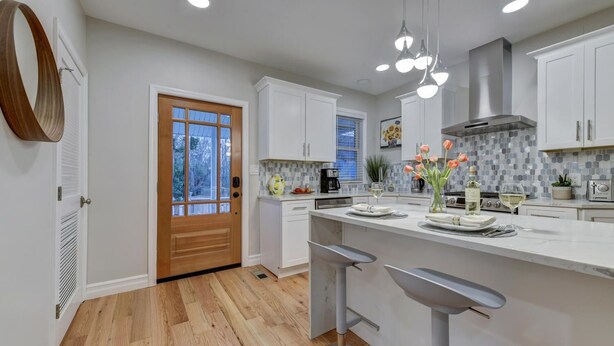A modern kitchen with white cabinets, a wooden door, and a tiled backsplash.