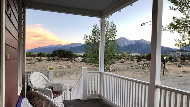 A covered porch with wicker chairs, a view of mountains, and a clear sky.