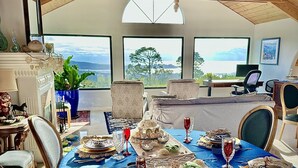 A dining area with a long table set for a meal, large windows with a view, and a high wooden ceiling. - PRIVATE Hilltop Home: Stunning Carmel Views, Hot Tub, 3 Balconies, Espresso (Carmel-By-The-Sea)