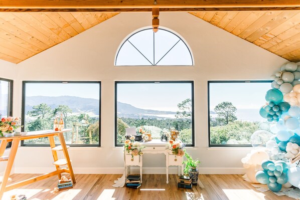 Una habitación con amplios ventanales, techo de madera y un escritorio con objetos decorativos.