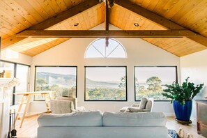 Amplio salón con techo alto, ventanas grandes que ofrecen vistas a un puente y follaje, y una zona de estar acogedora.