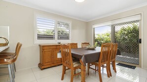 A dining area with a table, chairs, a wooden cabinet, and a window with blinds. - 44 Oaks Avenue, No:4 (Long Jetty)