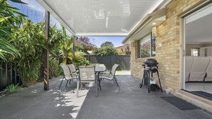 An outdoor patio with a table and chairs, a barbecue grill, and a covered area with a view of the garden. - 44 Oaks Avenue, No:4 (Long Jetty)