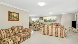 A spacious living room with two patterned sofas, a leather recliner, a dining area with a table and chairs, and a large window providing natural light. - 44 Oaks Avenue, No:4 (Long Jetty)
