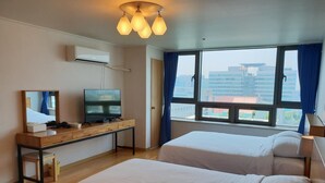 Habitación de hotel con dos camas, un televisor sobre un escritorio de madera y un ventanal con vista a la ciudad.