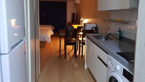 Una habitación de hotel compacta con kitchenette, una cama, un escritorio y una lavadora.