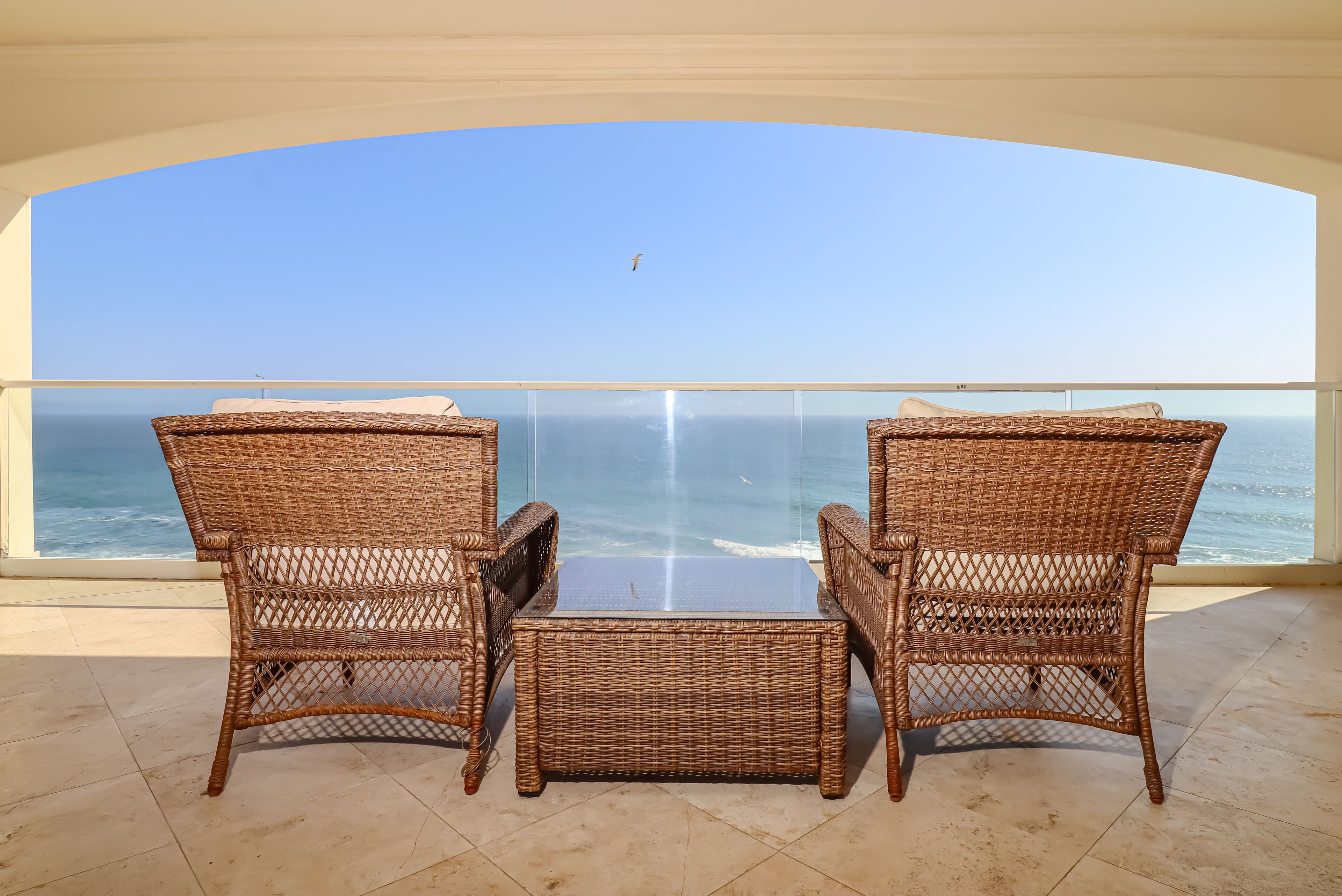 A balcony with wicker furniture overlooking the sea.