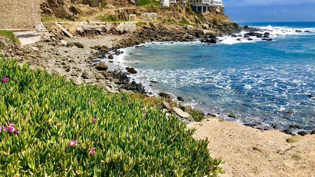 Uma propriedade costeira com linha costeira rochosa, uma praia arenosa e um penhasco com edifícios.