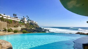 Piscina azul límpida com vista para o oceano e um edifício com janelas em arco.