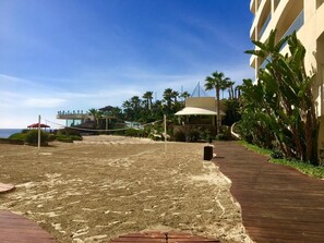A beach volleyball court with a net, palm trees, and a building in the background. - VacationCondo-LasOlasGrand-Pools&Jacuzzis-Rosarito (Playas de Rosarito)