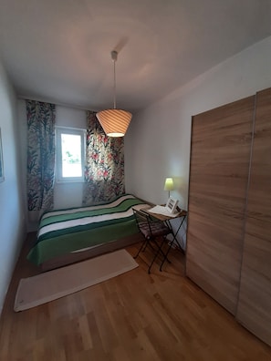 Une chambre à coucher avec un lit, un bureau avec une lampe, une fenêtre et une armoire.