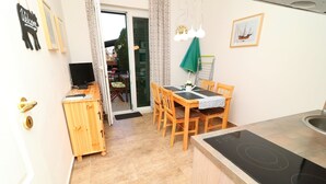 A compact kitchen with a dining area, a wooden cabinet, a black TV, and a sliding glass door leading to a balcony.