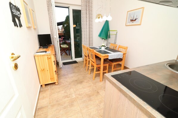 Une cuisine compacte avec un coin repas, un meuble en bois, un téléviseur noir et une porte-fenêtre coulissante donnant sur un balcon.