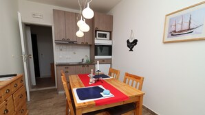 A compact kitchen with modern appliances, a dining area with a red table runner, and a framed picture on the wall. - Apartments Trstenica-One Bedroom Apartment with Balcony (Orebic)