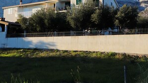 Una casa de dos pisos con balcón, rodeada de árboles y montañas al fondo.