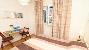 A bedroom with a bed, a desk, two chairs, a lamp, and a window with curtains. - Apartments Trstenica-One Bedroom Apartment with Balcony (Orebic)