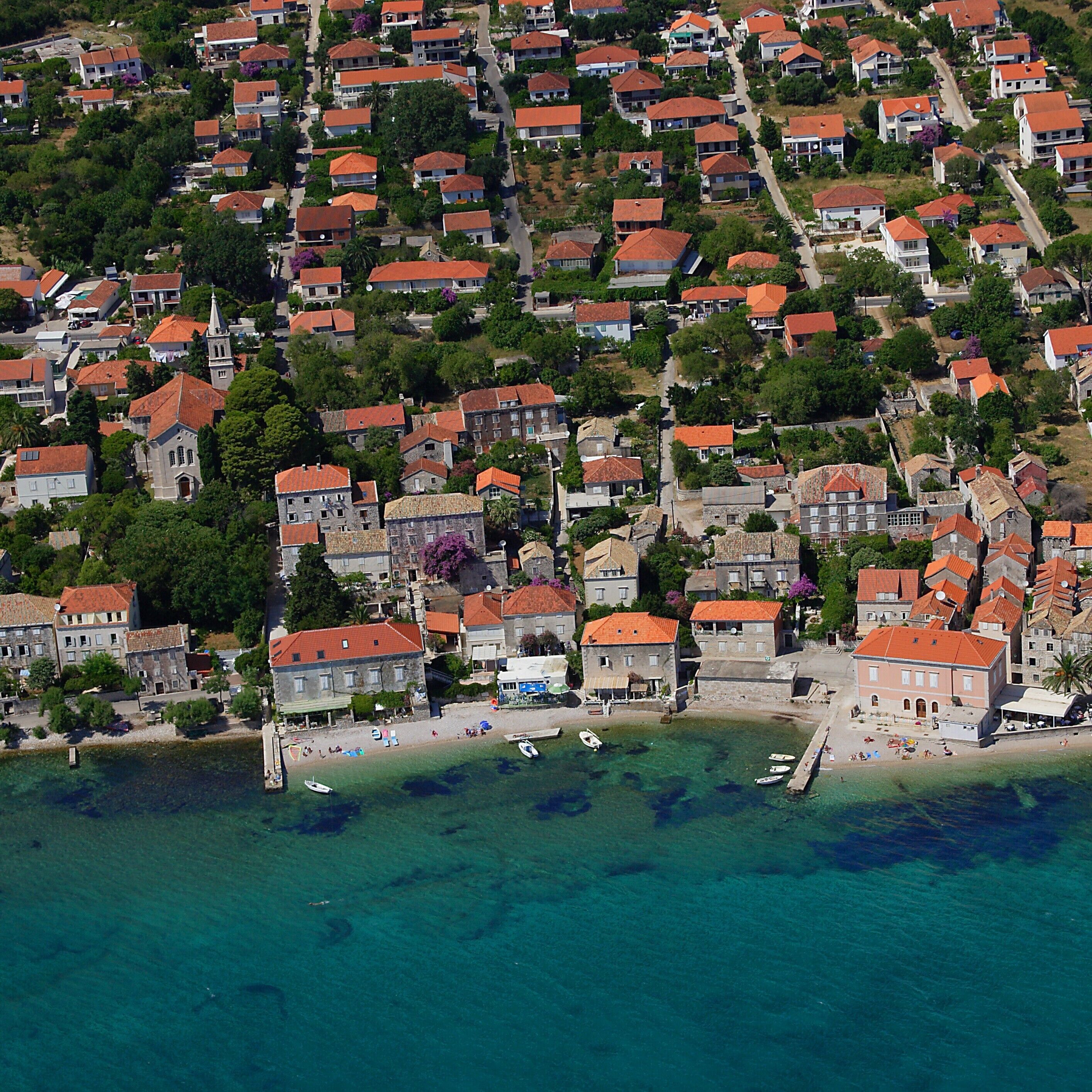 An aerial view of a coastal town with terraced houses, a central square, and a beach with boats.