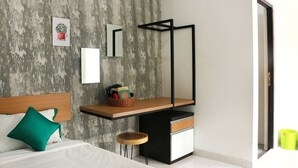 A modern bedroom with a bed, a bedside table, a small stool, and a desk with a chair. - Hotel Kili Suci by Simply Homy (Yogyakarta)