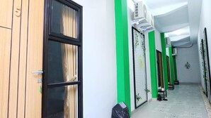 A hallway with green and white walls, a wooden door, and a trash bin. - Hotel Kili Suci by Simply Homy (Yogyakarta)