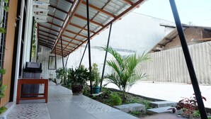 A covered outdoor area with a tiled floor, potted plants, and a wooden bench. - Hotel Kili Suci by Simply Homy (Yogyakarta)