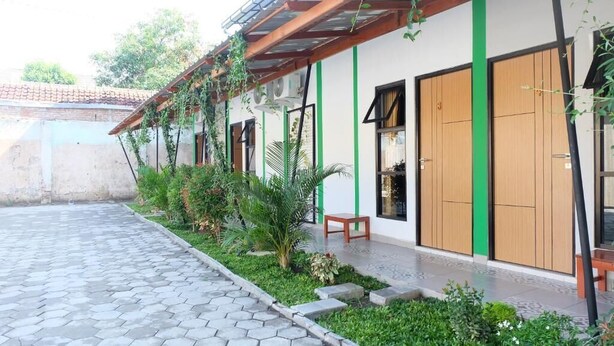 A building with a covered patio area, green plants, and a tiled walkway. - Hotel Kili Suci by Simply Homy (Yogyakarta)