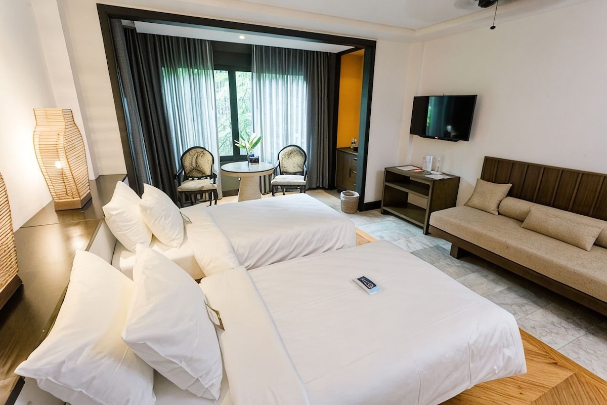 Ein Hotelzimmer mit zwei Betten, einem Sofa, einem Fernseher und einer Essecke mit Stühlen und einem Tisch.