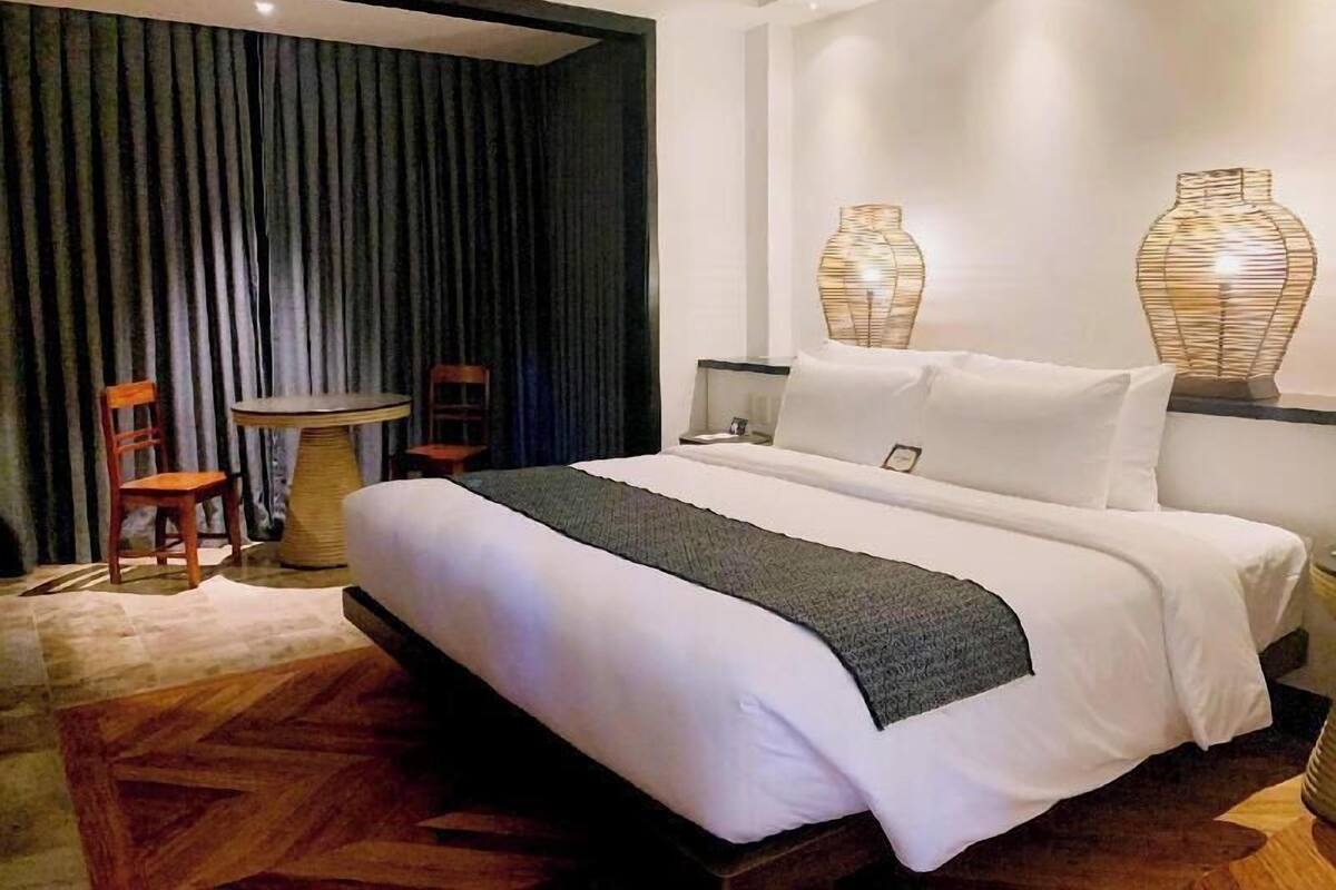 Una habitación de hotel con una cama, dos sillas, una mesita y dos lámparas de pared.