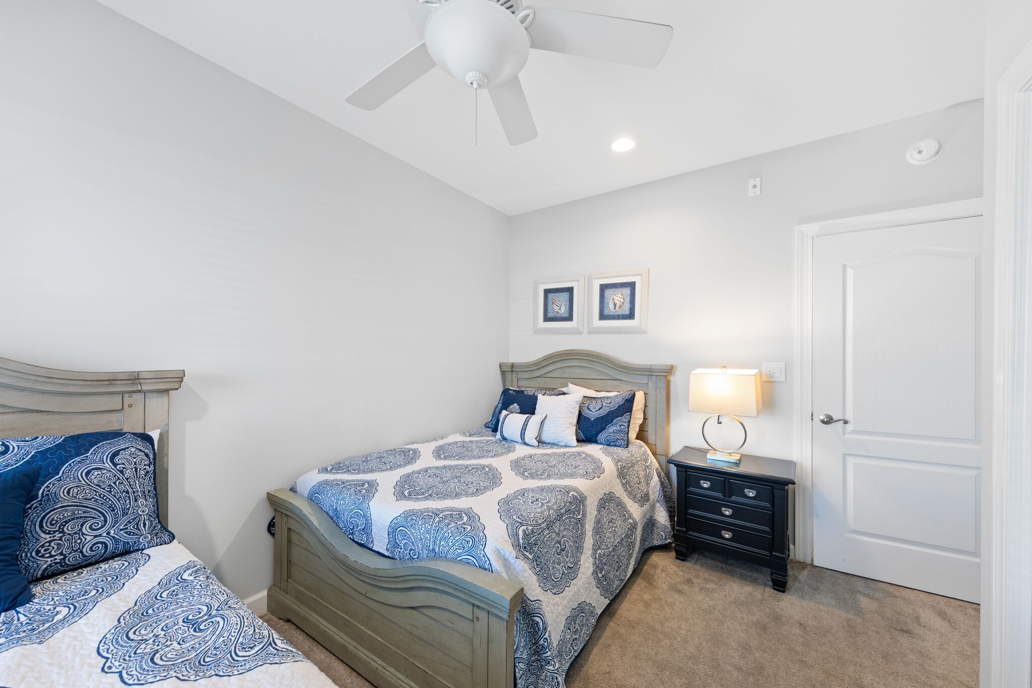 A bedroom with a bed, a nightstand, a ceiling fan, and a door.