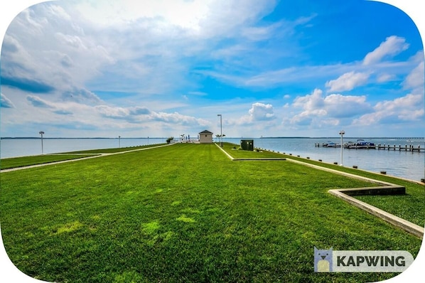 A well-maintained grassy area with a small building and a dock extending into the water.