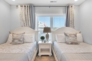 Un dormitorio con dos camas, una mesita de noche con lámpara y una ventana con cortinas.