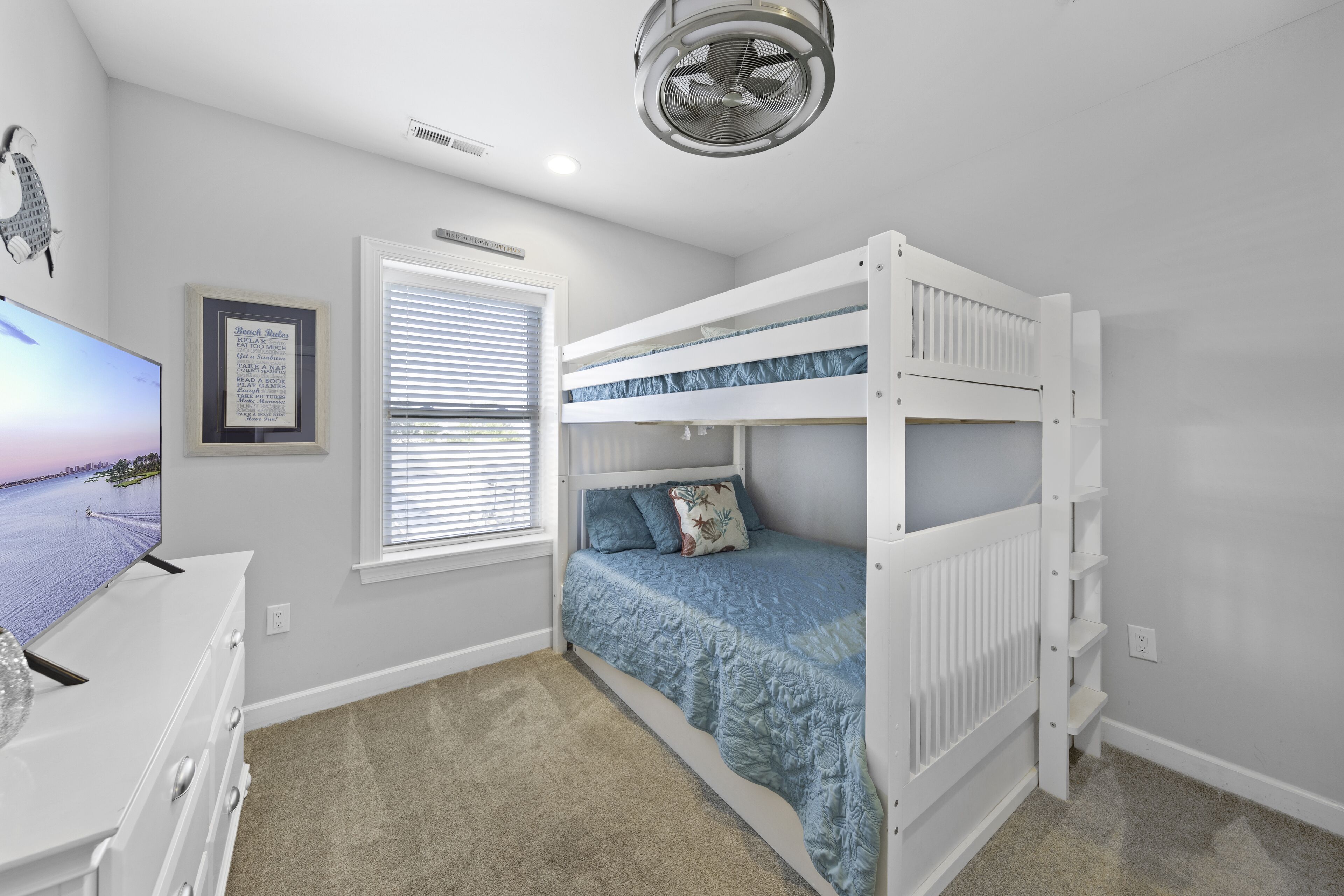 A bedroom with bunk beds, a desk, a framed picture, and a window with blinds.