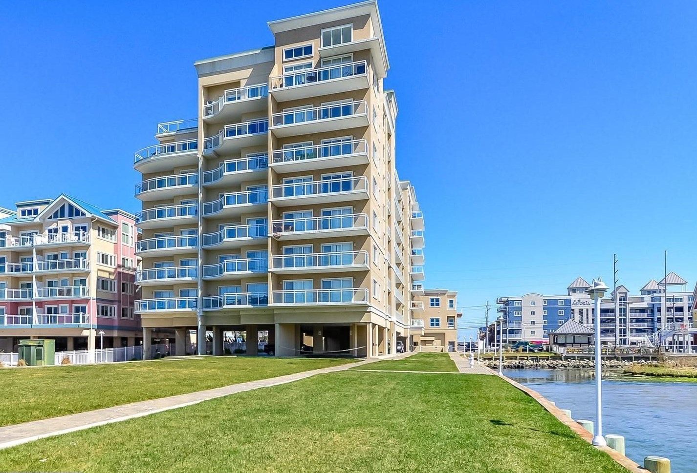 A multi-story hotel with balconies, a grassy area in front, and a body of water nearby.