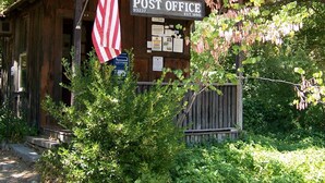 Un bureau de poste en bois, orné d’un drapeau américain, entouré de verdure.