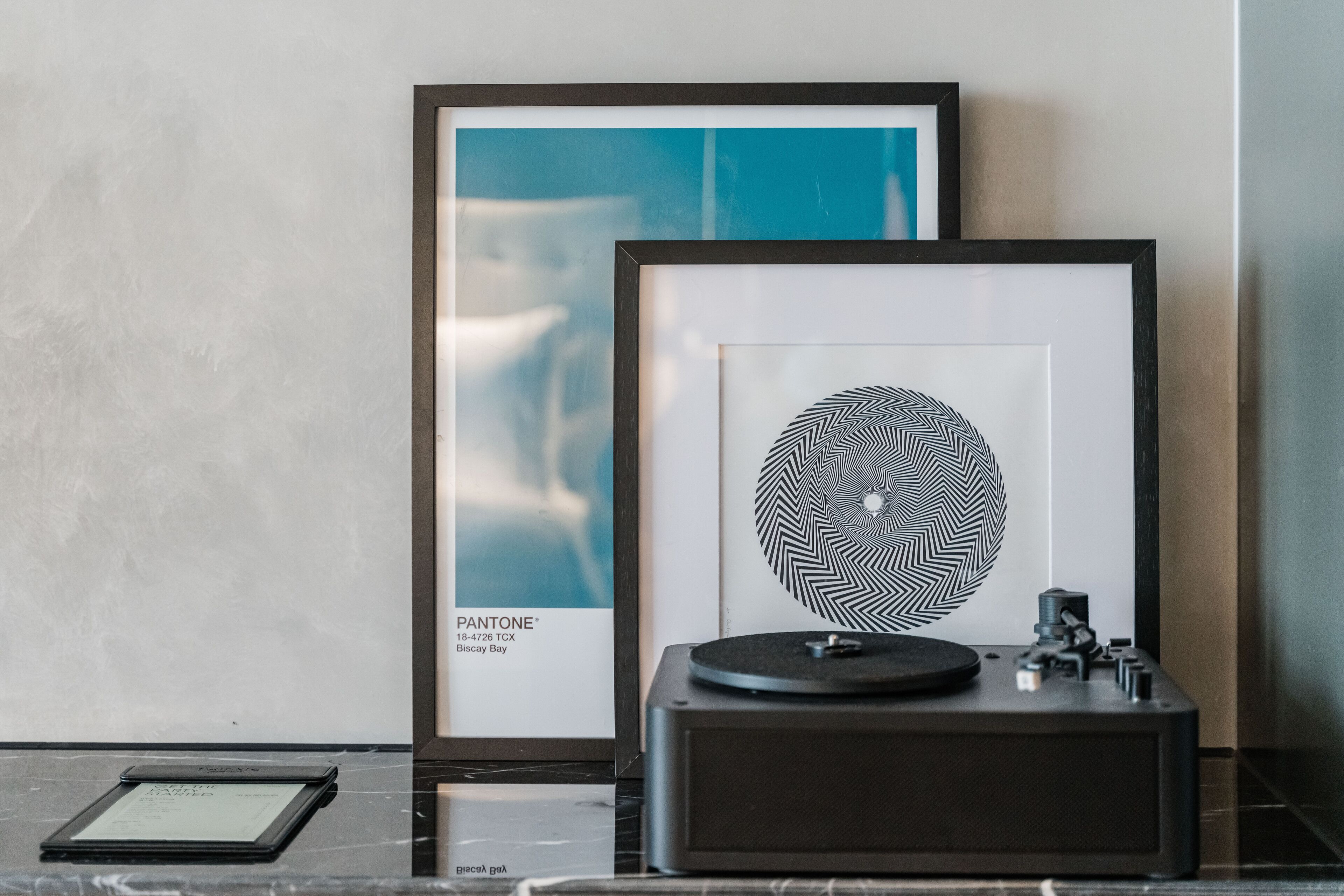 A framed artwork, a turntable, and a tablet on a marble surface.