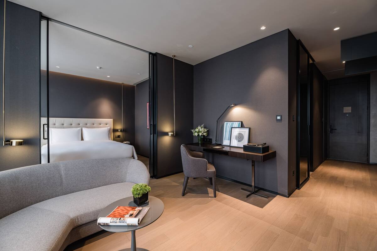 Una habitación de hotel moderna con una cama, un escritorio, una silla, una mesita con una planta y un sofá.