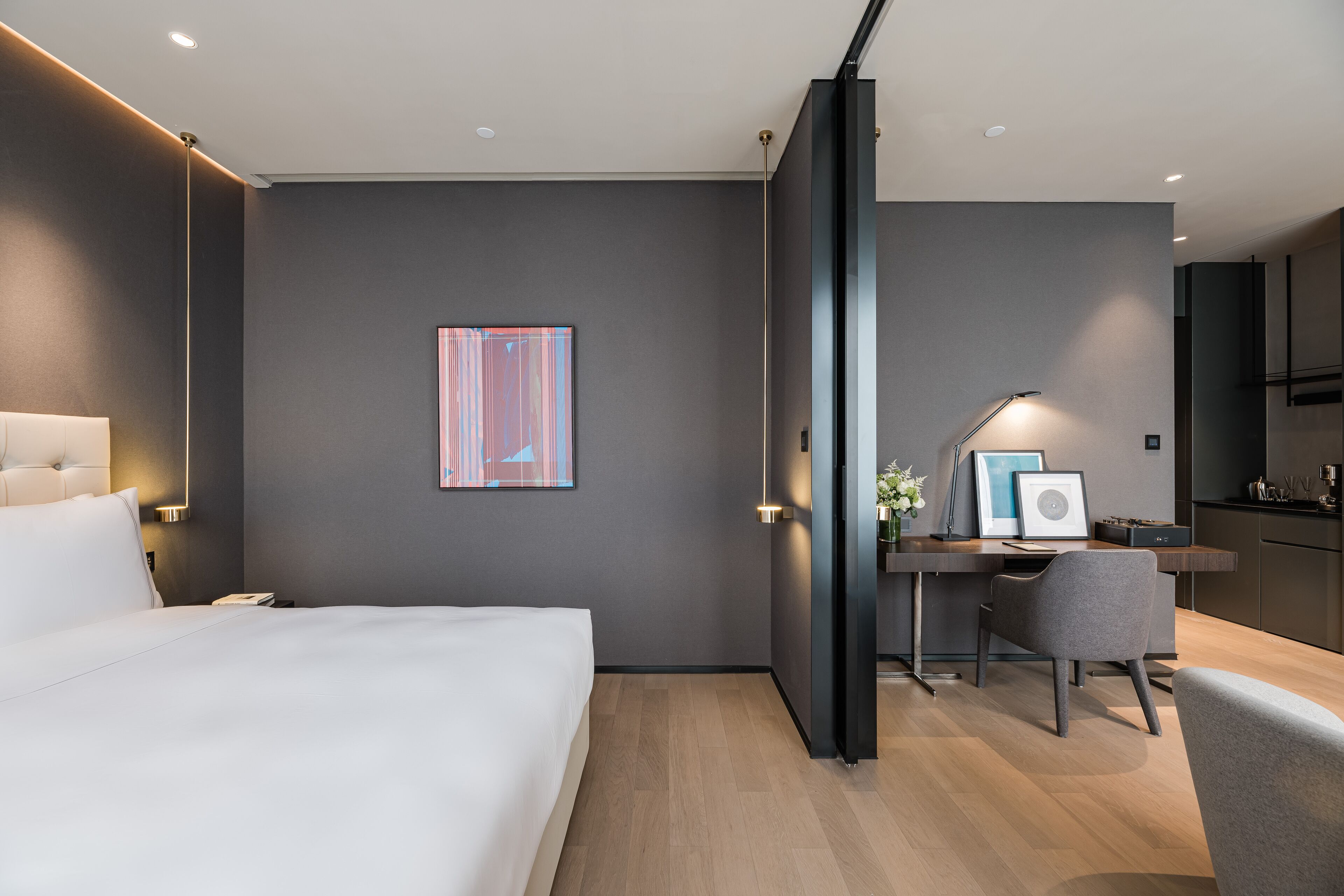 A modern hotel room with a bed, desk, chair, and artwork on the wall.