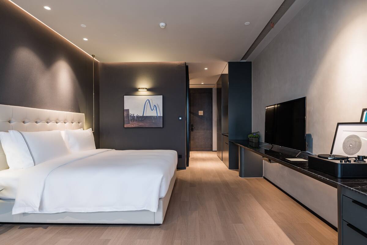 Una habitación de hotel moderna con una cama grande, un televisor de pantalla plana, una pequeña cocina y un cuadro enmarcado en la pared.