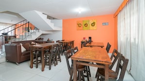 Ein Essbereich mit Holztischen und -stühlen, einer Treppe und einer Wand in Orange.