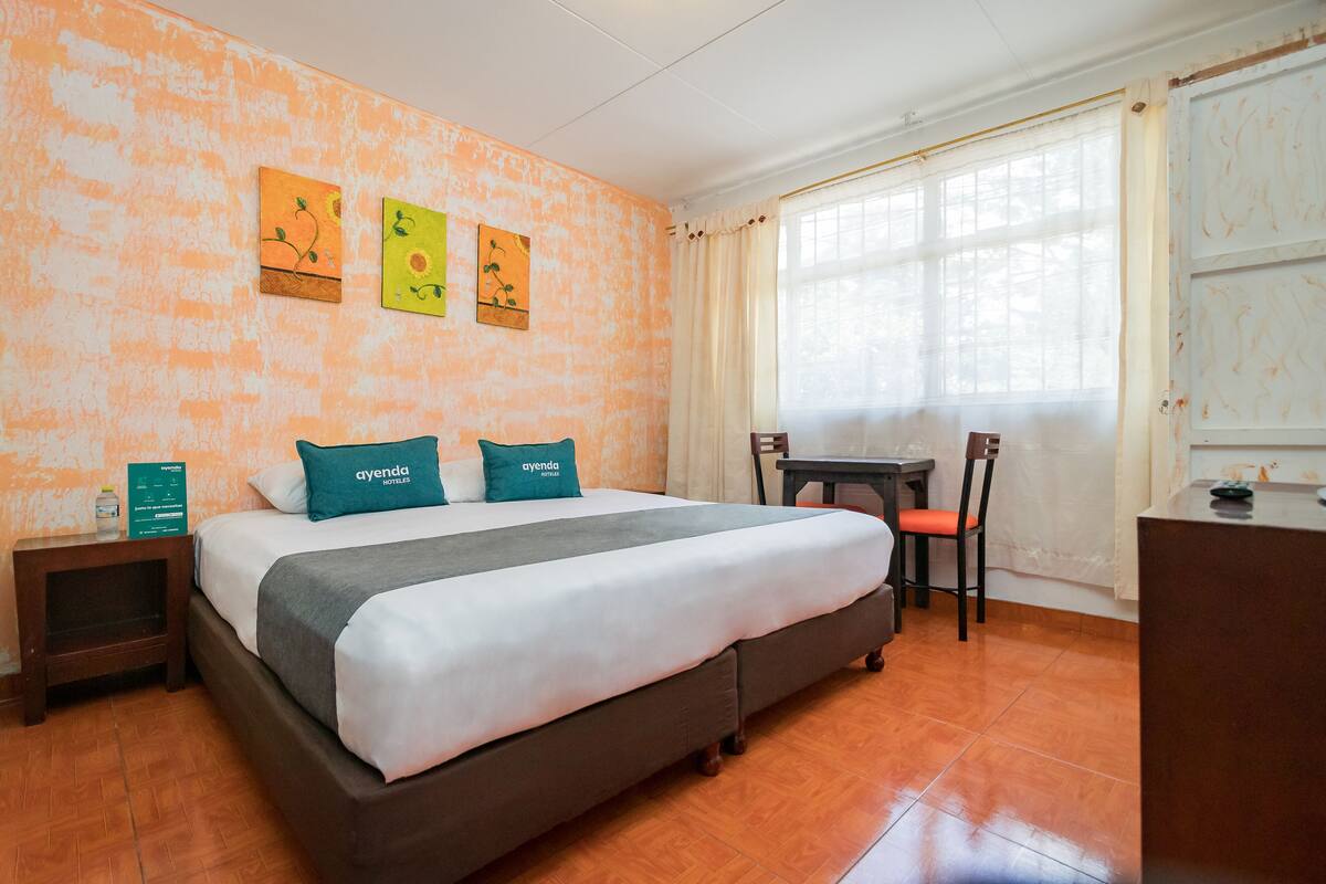 Habitación de hotel con una cama, un escritorio y una silla. Hay tres cuadros en la pared.