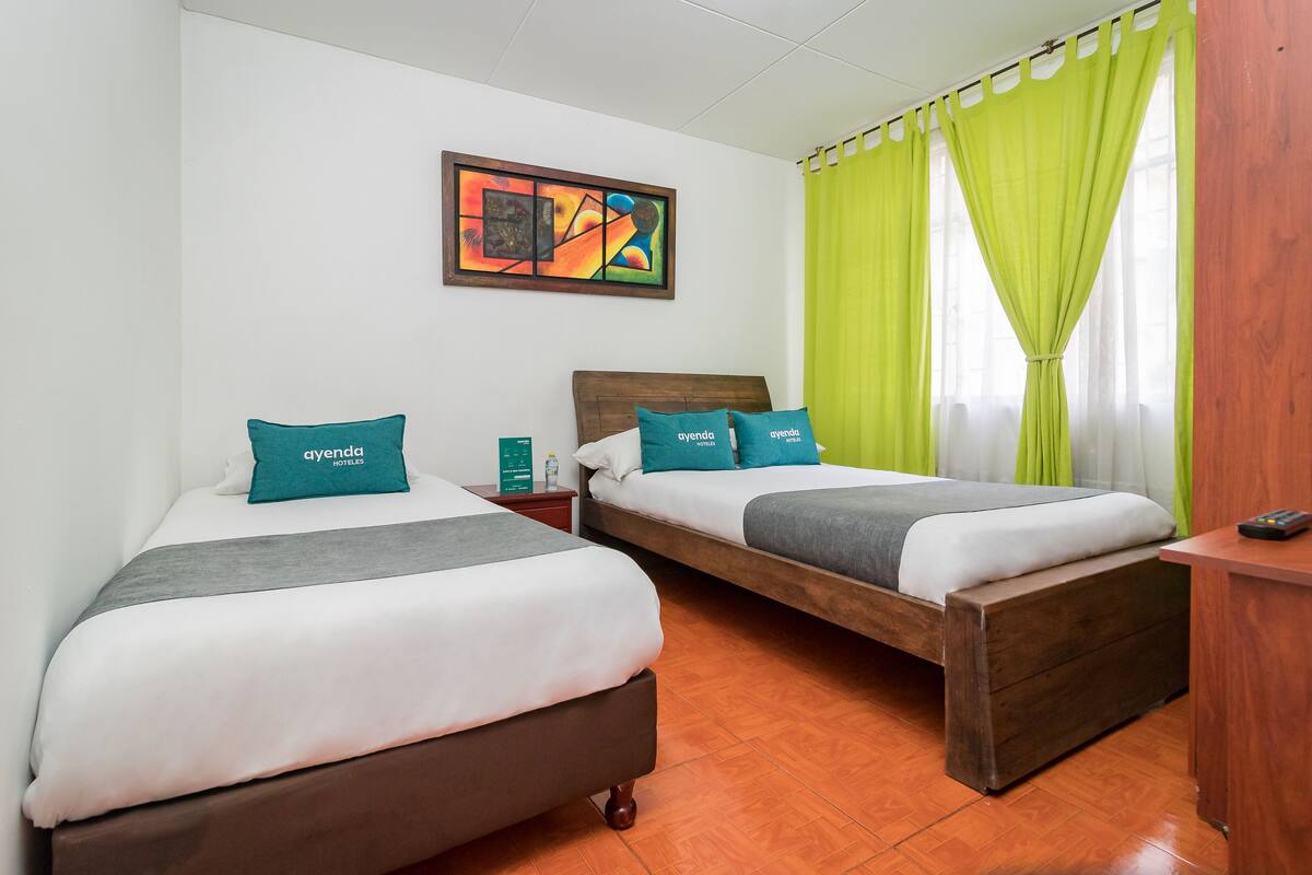 Habitación de hotel con dos camas, un cuadro en la pared y una ventana con cortinas verdes.