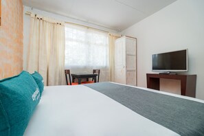 Habitación de hotel con cama, televisor en un mueble, una mesa de comedor con sillas y una ventana con cortinas.