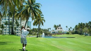 A golf course with a building in the background, palm trees, and a clear sky. - Mayan Palace In Acapulco inside Vidanta Resort Luxury in your services (Acapulco)